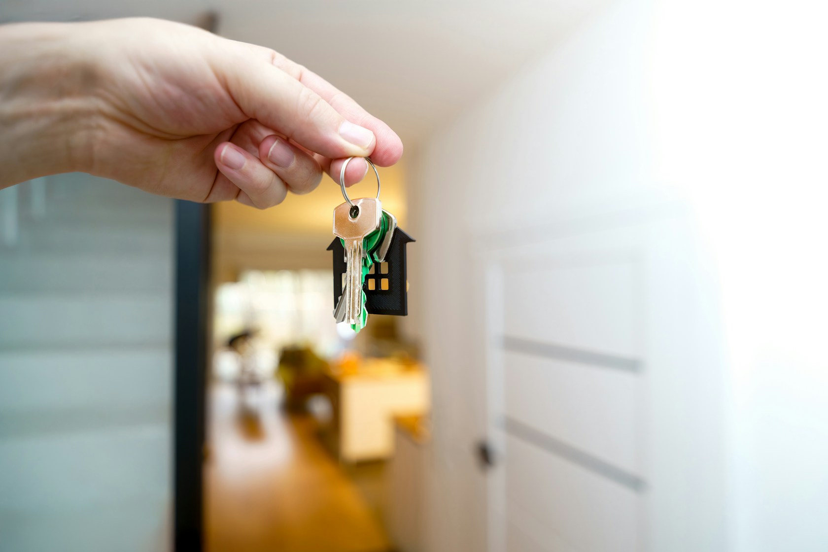 Préstamo hipotecario: mano sosteniendo las llaves de una vivienda frente a la puerta de entrada