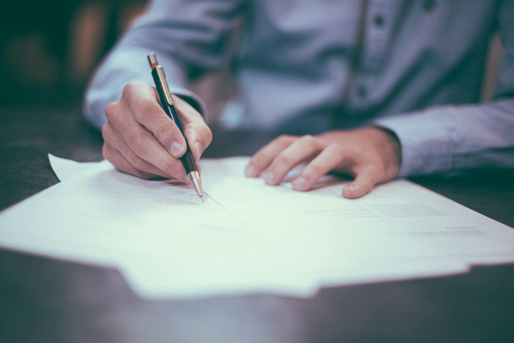 Mano firmando un documento con bolígrafo sobre un escritorio de oficina