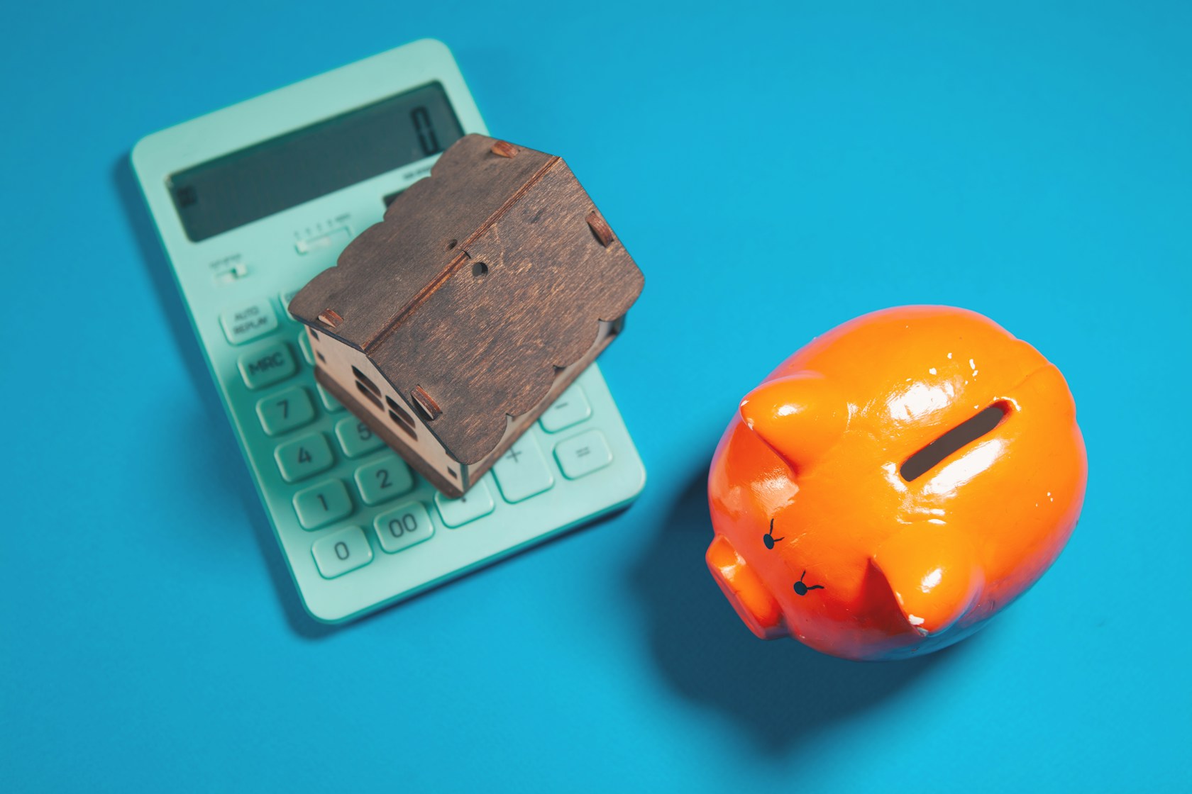 Carencia en la hipoteca: maqueta de casa sobre una calculadora junto a una hucha naranja