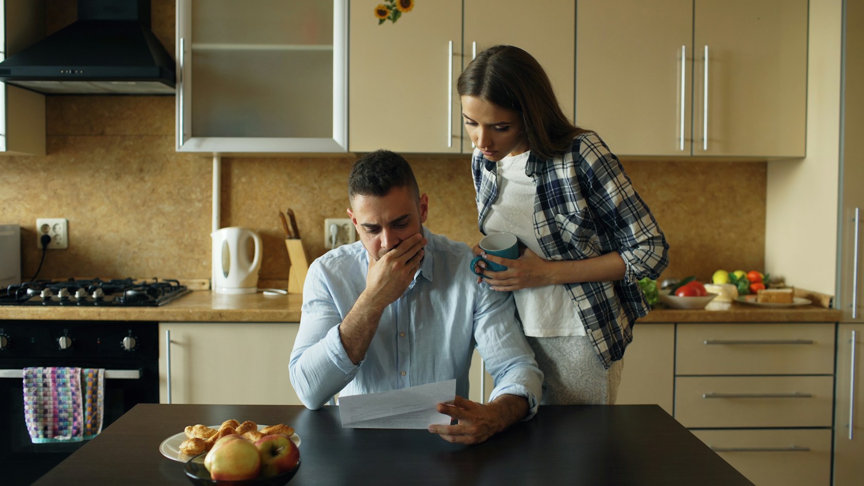 Código de Buenas Prácticas hipotecario: pareja preocupada revisando en la cocina una carta sobre la cuota de su hipoteca