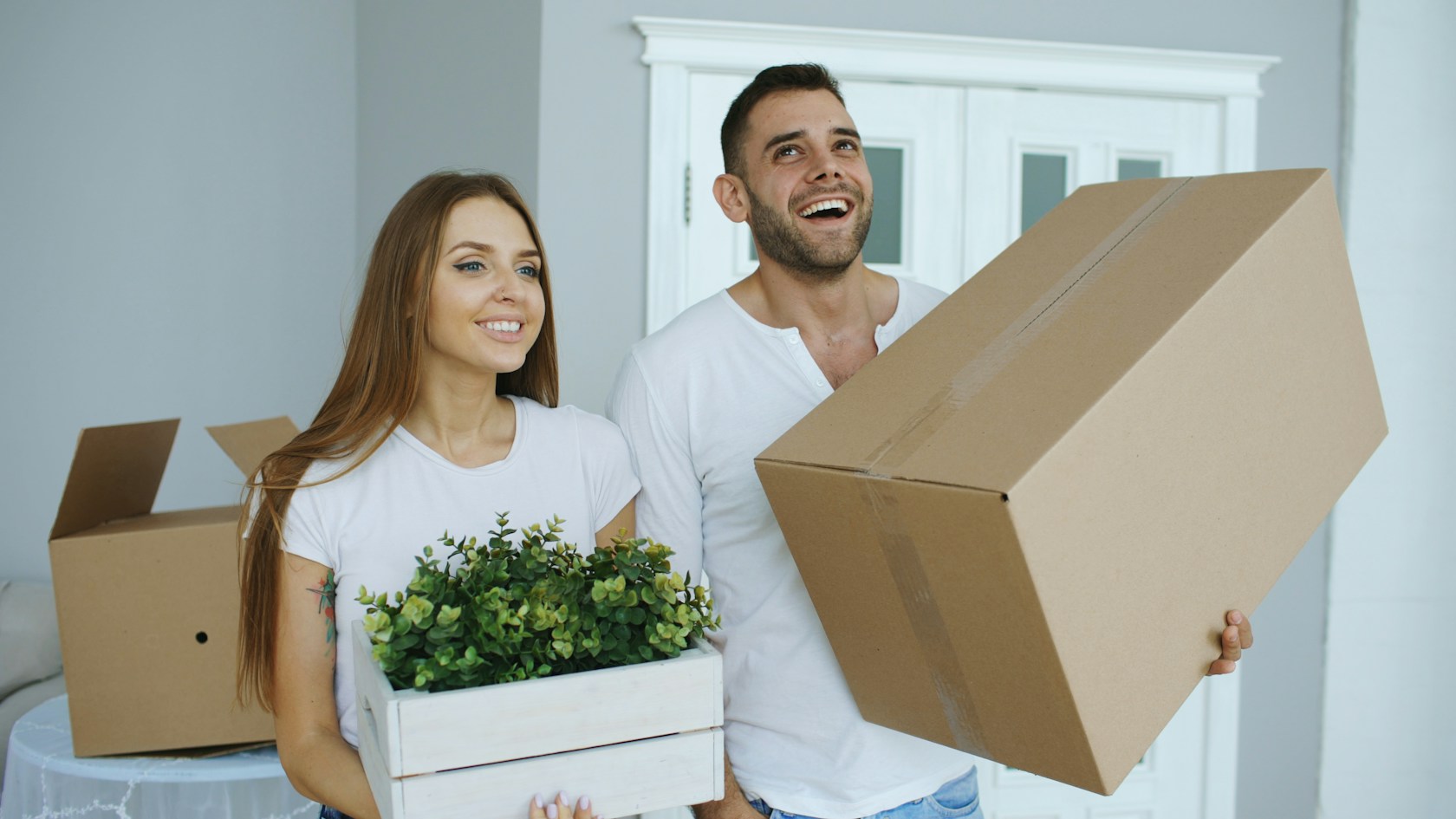 Hipoteca joven: pareja joven con cajas de mudanza y una planta en su primera vivienda